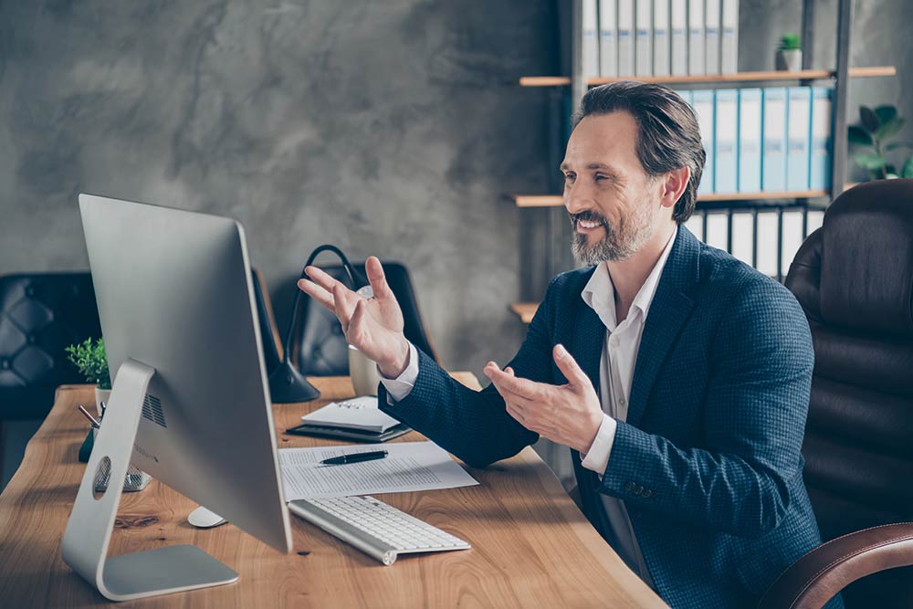 Man at desktop in front of monoítor explaining something