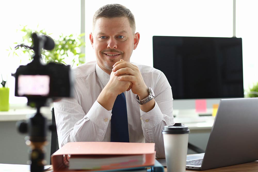 Man at desktop lokking into a camera which is streaming