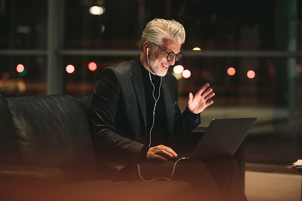 Man with earphone in a hotel lobby waving hello into creen before him