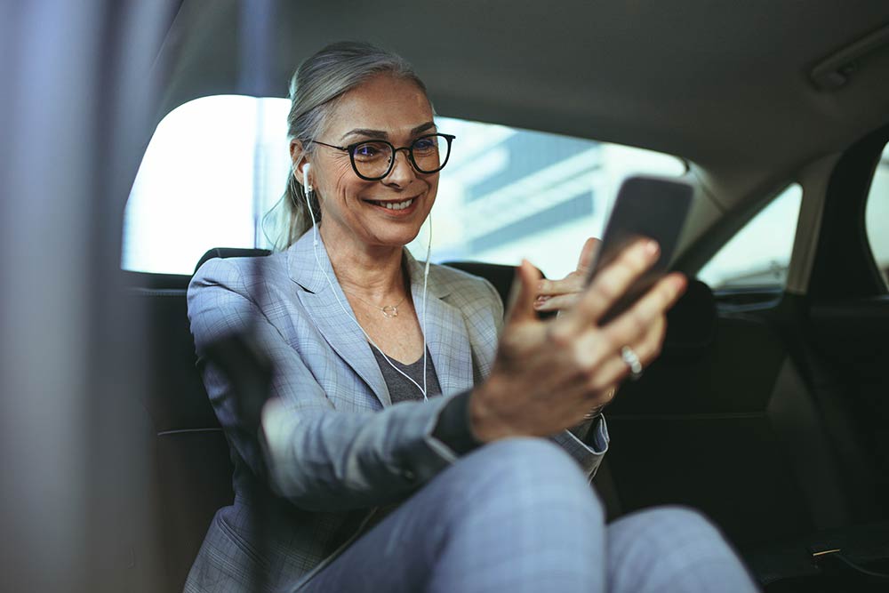 woman in a the backseat of a limosine talking via video on a smartphone